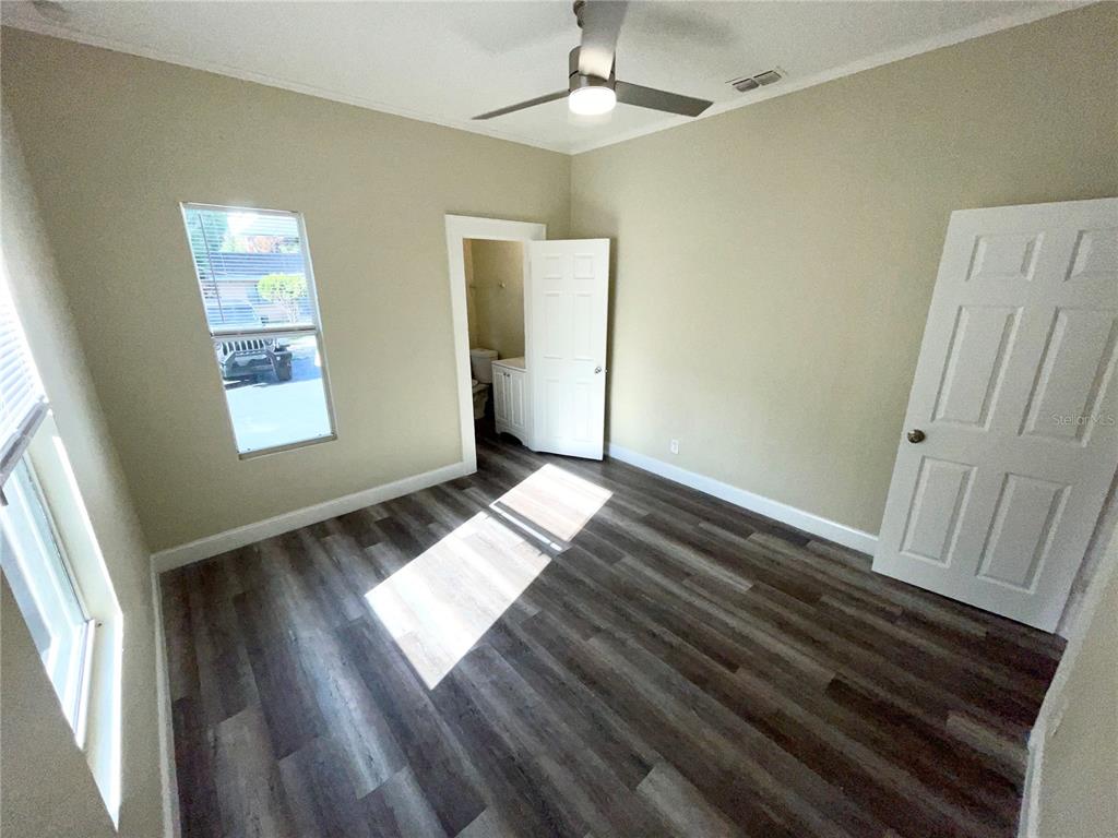 A bedroom with light-colored walls, wood-look flooring, a ceiling fan, and an attached bathroom — 1121 10TH AVENUE S, ST PETERSBURG, FL