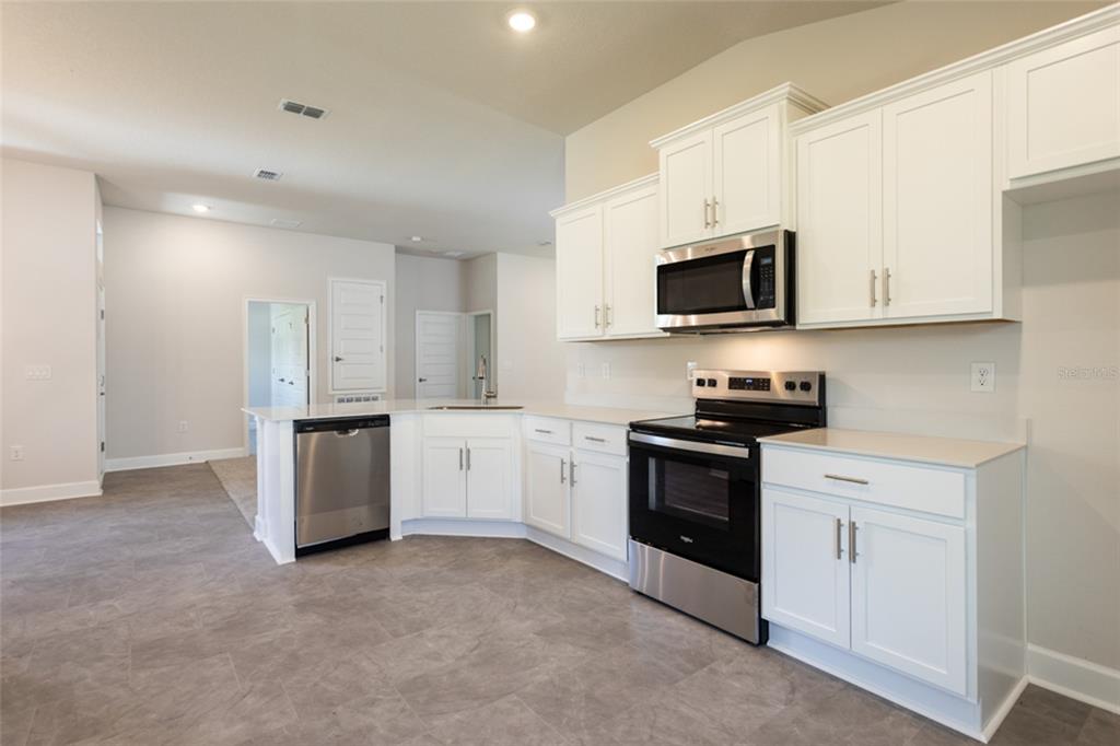 A kitchen features white cabinets, stainless steel appliances, and gray tile flooring — 79 PORT ROYAL DRIVE, PALM COAST, FL