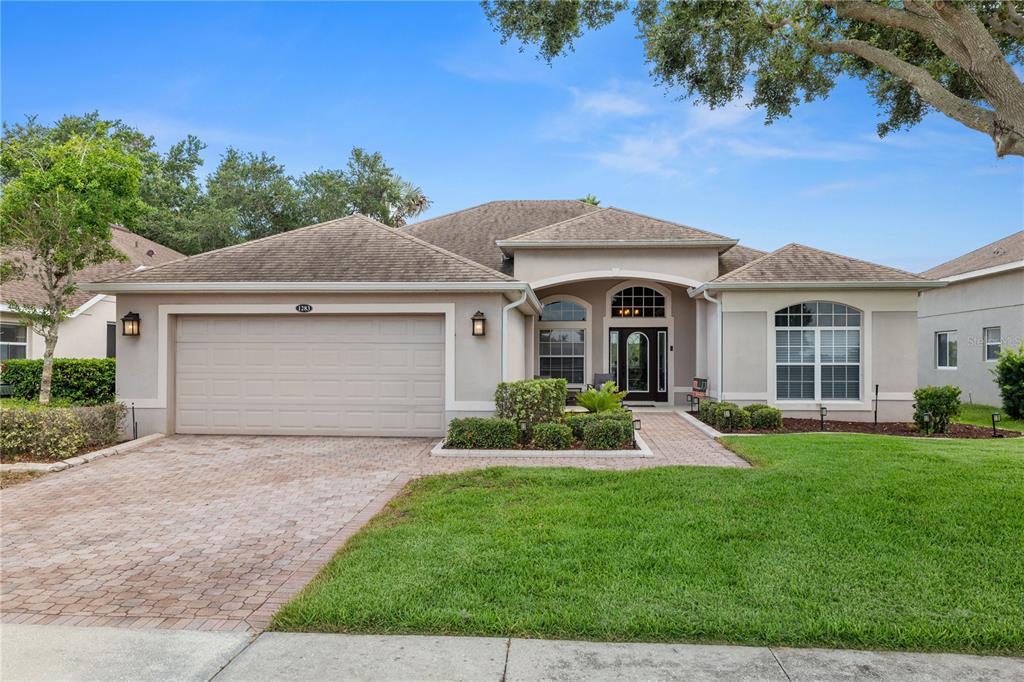A single-story house with a beige stucco exterior, a brick driveway, and a two-car garage — 1283 LEGENDARY BOULEVARD, CLERMONT, FL