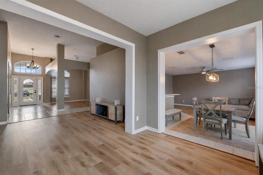 An open-concept living area features light wood-look flooring, neutral walls, and a dining space — 1283 LEGENDARY BOULEVARD, CLERMONT, FL