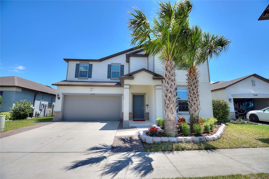 A two-story suburban house features a two-car garage, a front porch, and two palm trees — 17244 GOLDCREST LOOP, CLERMONT, FL