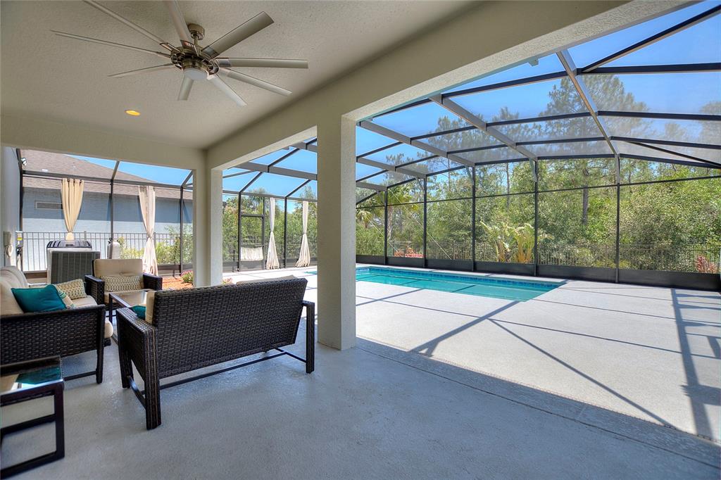 A covered patio features outdoor furniture, a ceiling fan, and a screened-in swimming pool area — 17244 GOLDCREST LOOP, CLERMONT, FL