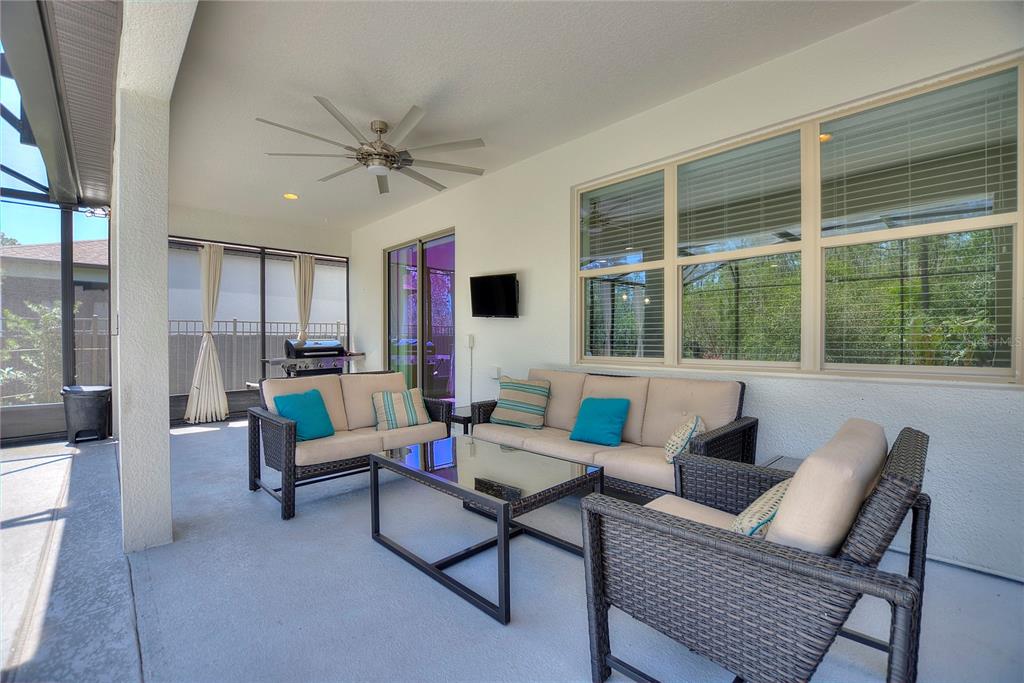 A covered patio features wicker furniture, a ceiling fan, a wall-mounted television, and screen enclosures — 17244 GOLDCREST LOOP, CLERMONT, FL