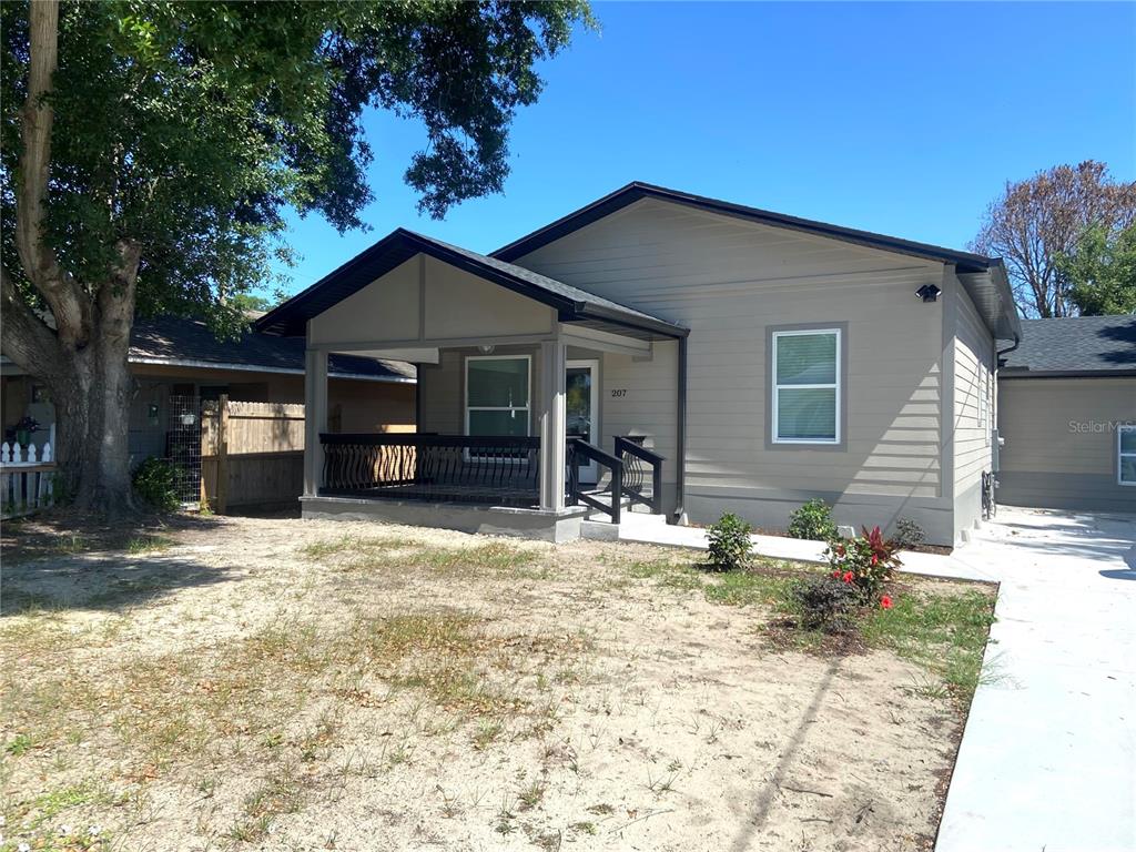 A single-story house with a covered front porch, tan siding, and a concrete driveway — 207 AVENUE E SE, WINTER HAVEN, FL