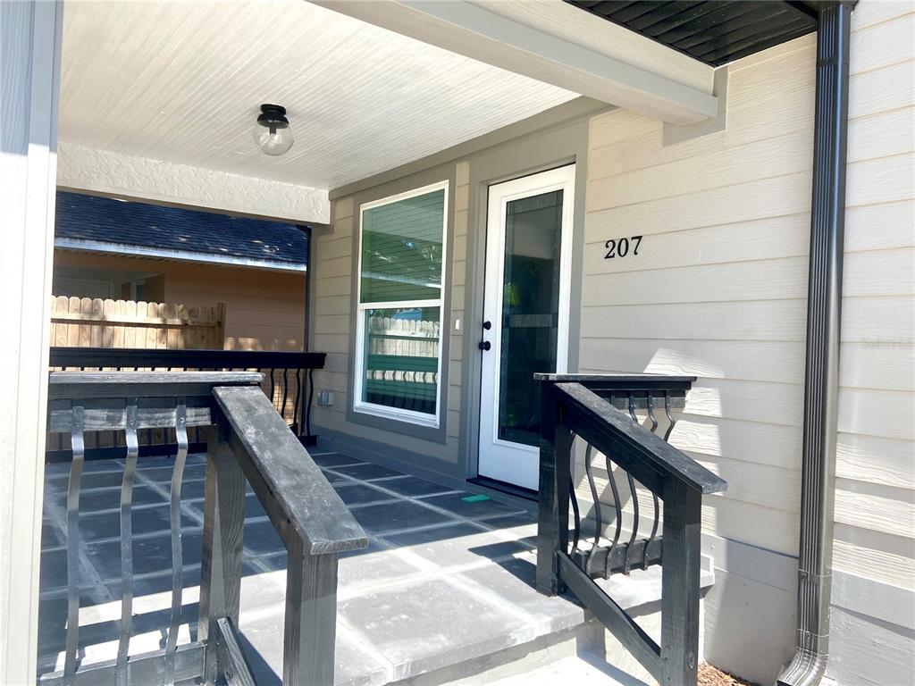 A covered porch features a white door, black railings, and gray tiled flooring — 207 AVENUE E SE, WINTER HAVEN, FL