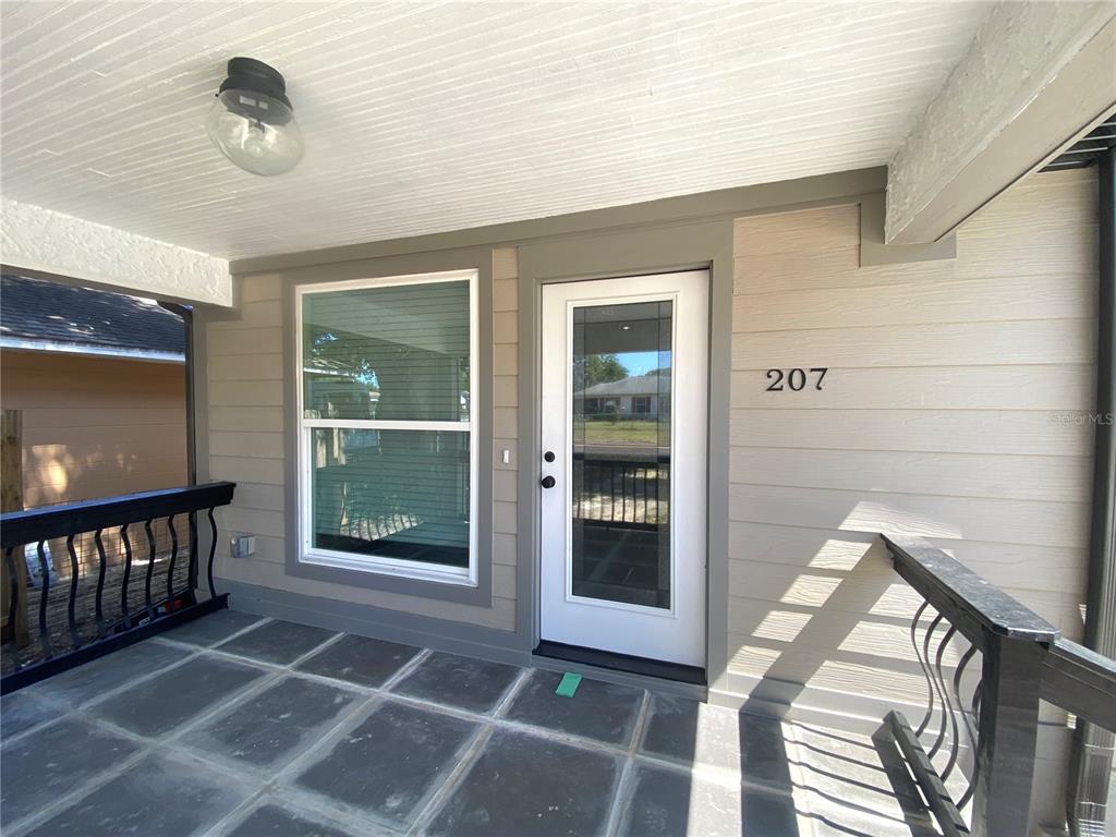 A covered porch features a white front door, large window, and dark tiled flooring — 207 AVENUE E SE, WINTER HAVEN, FL