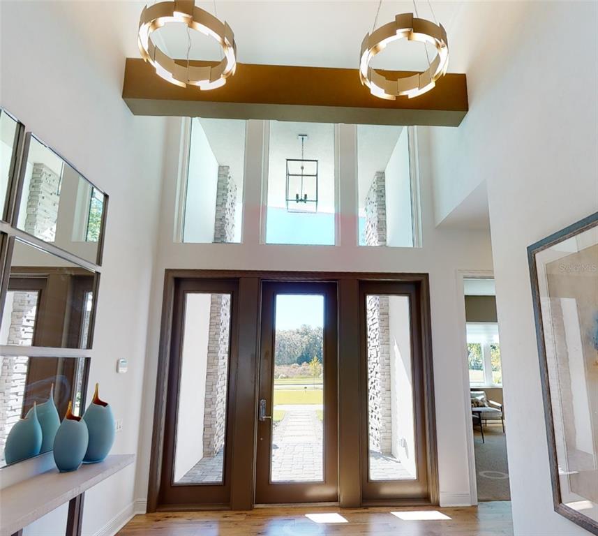 A bright entryway features a double-height ceiling, two modern ring chandeliers, and a glass-paneled door — 12364 SW 16TH LANE, NEWBERRY, FL