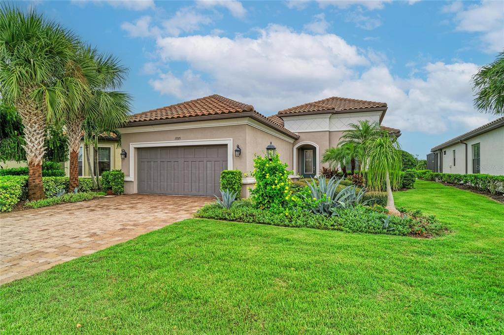 A single-story house with a tan stucco exterior, a tile roof, and a paved driveway — 13321 SORRENTO WAY, BRADENTON, FL