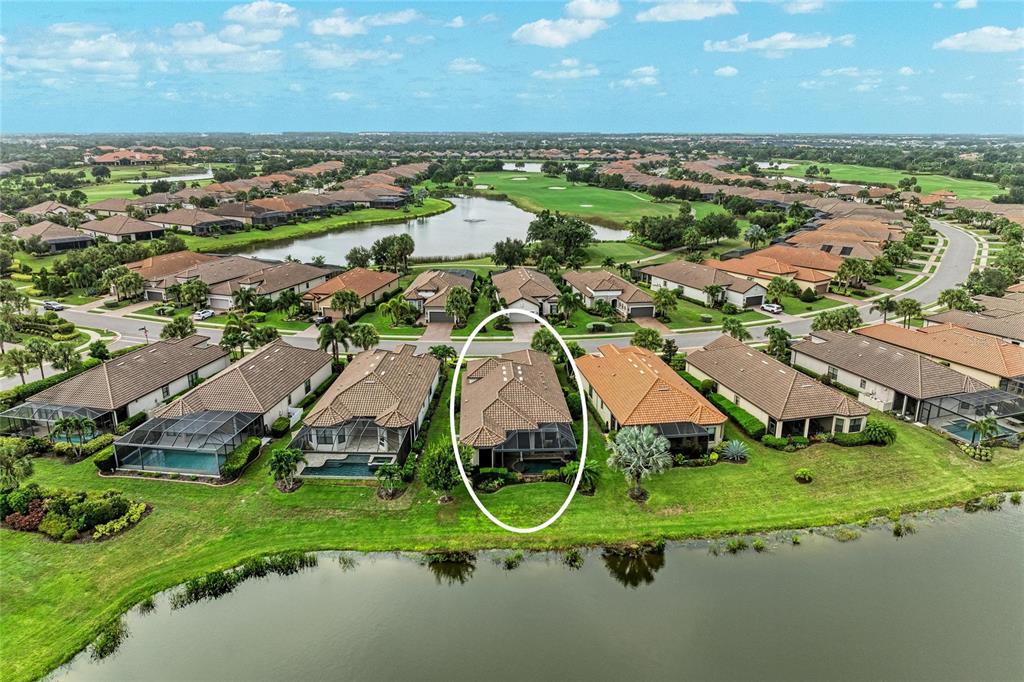 An aerial view shows a residential house with a pool enclosure situated by a lake — 13321 SORRENTO WAY, BRADENTON, FL