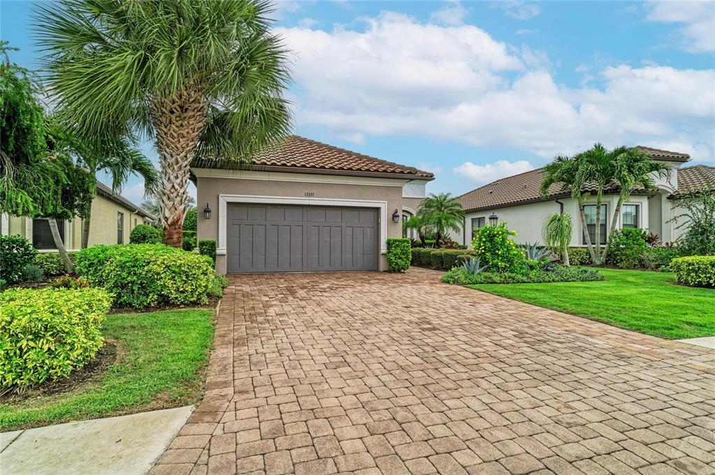 A paved driveway leads to the garage of a single-story house with a tiled roof — 13321 SORRENTO WAY, BRADENTON, FL
