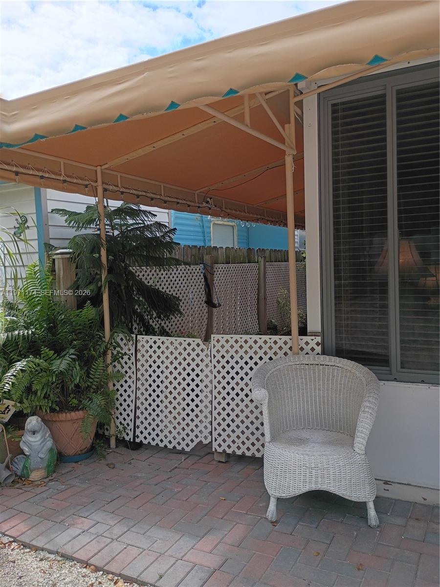 A white wicker chair sits on a brick patio under a tan metal awning — 101551 Overseas Hwy, 147, Key Largo FL 33037, KEY LARGO, FL