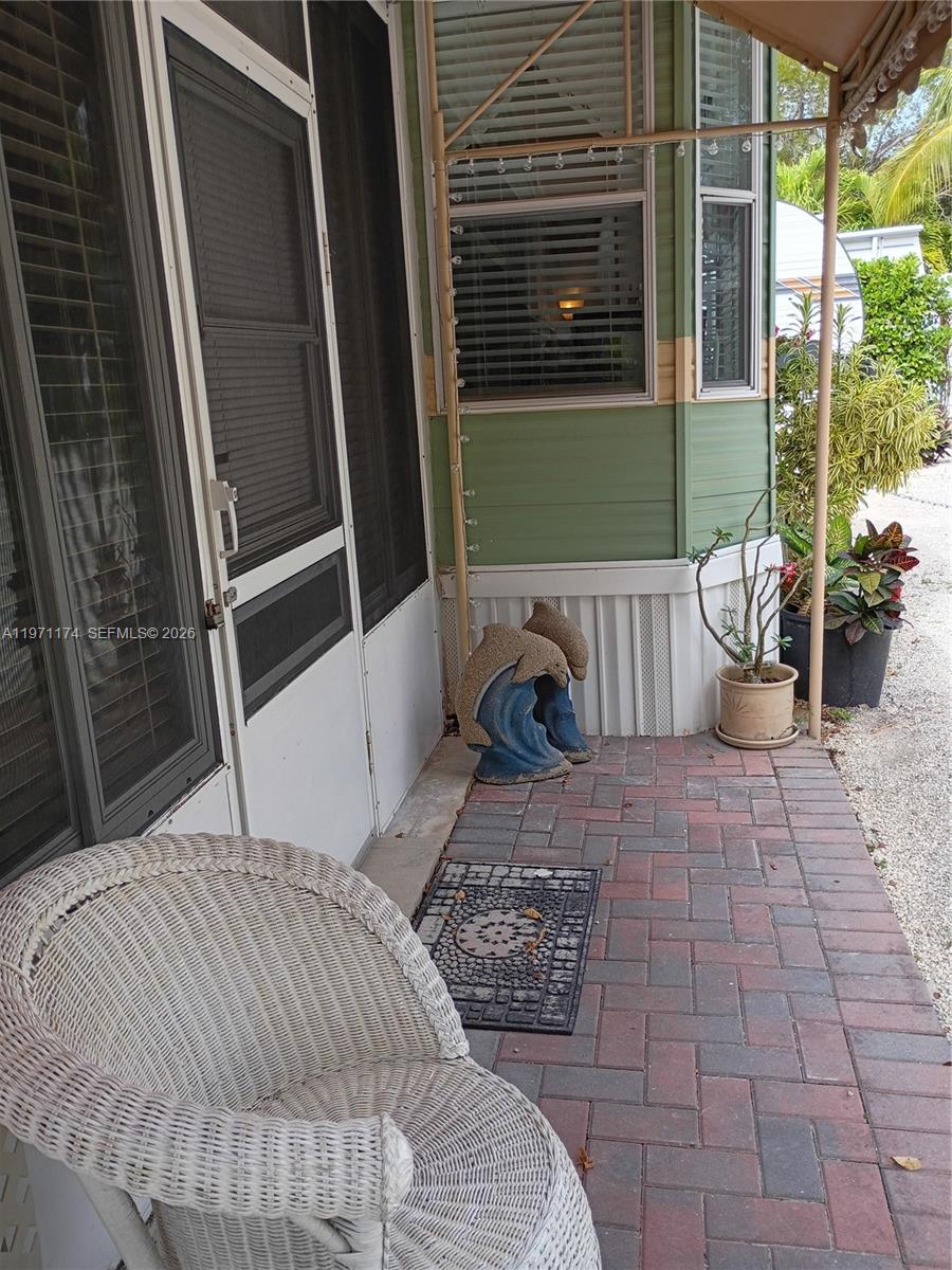 A white wicker chair sits on a brick patio beside a green mobile home entrance — 101551 Overseas Hwy, 147, Key Largo FL 33037, KEY LARGO, FL