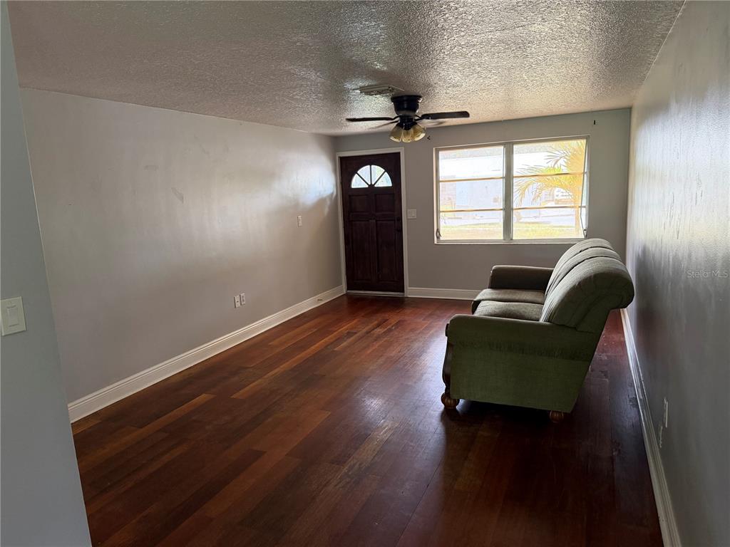 A living room features dark wood flooring, light gray walls, a ceiling fan, and a sofa — 6100 WYOMING AVENUE, NEW PORT RICHEY, FL
