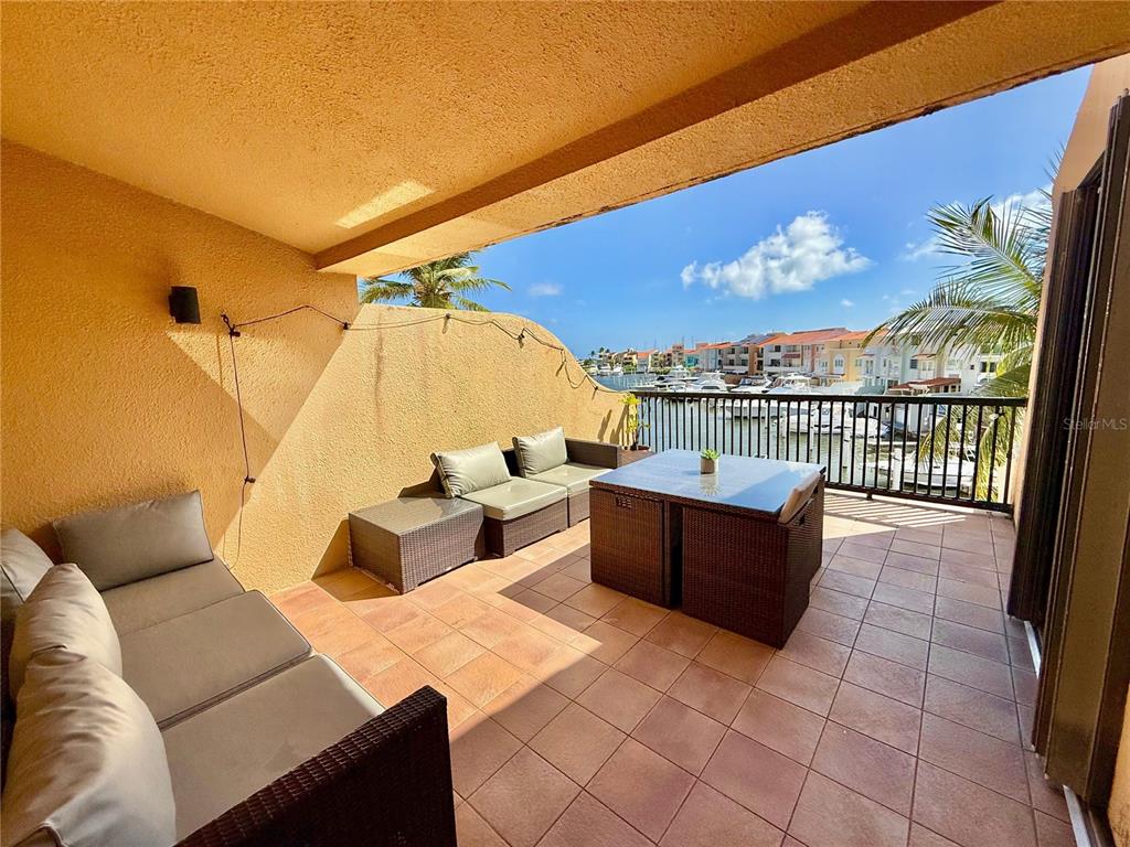 A covered balcony with outdoor furniture overlooks a marina with boats and waterfront buildings — 999 HARBOURSIDE UNIT 999, HUMACAO, PR