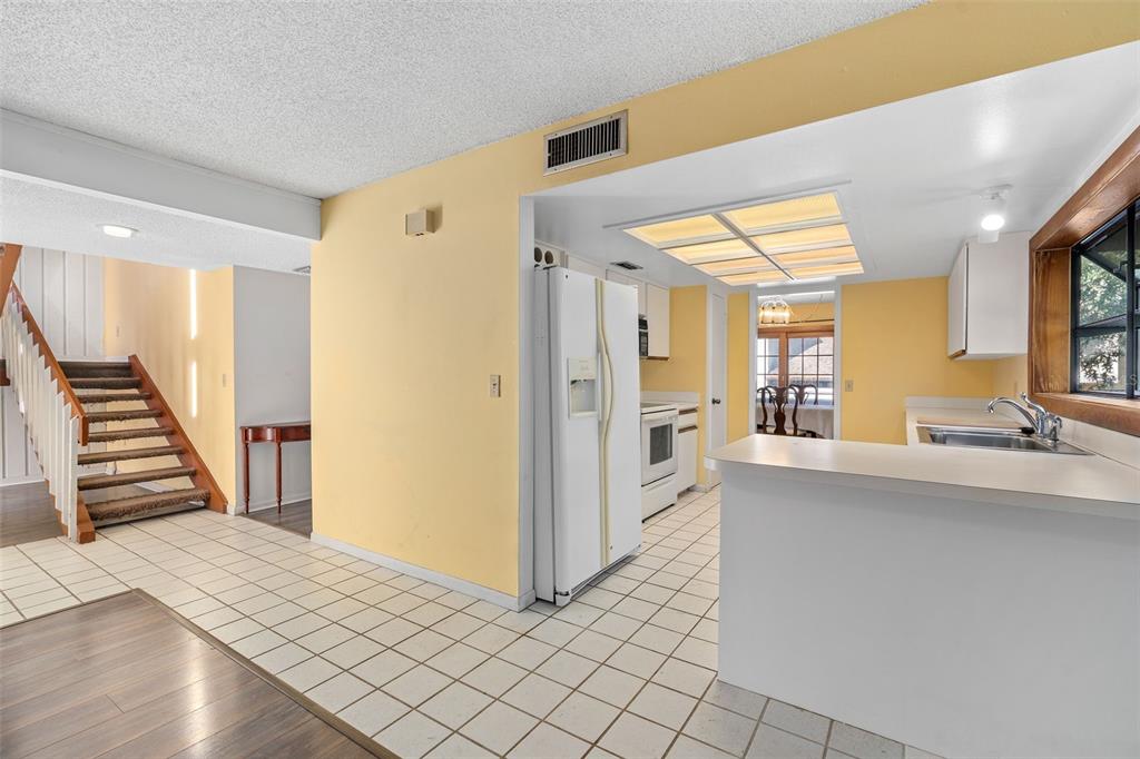 A kitchen with white appliances and cabinets opens to a tiled entryway and wooden staircase — 114 HIDDEN OAK DRIVE, LONGWOOD, FL