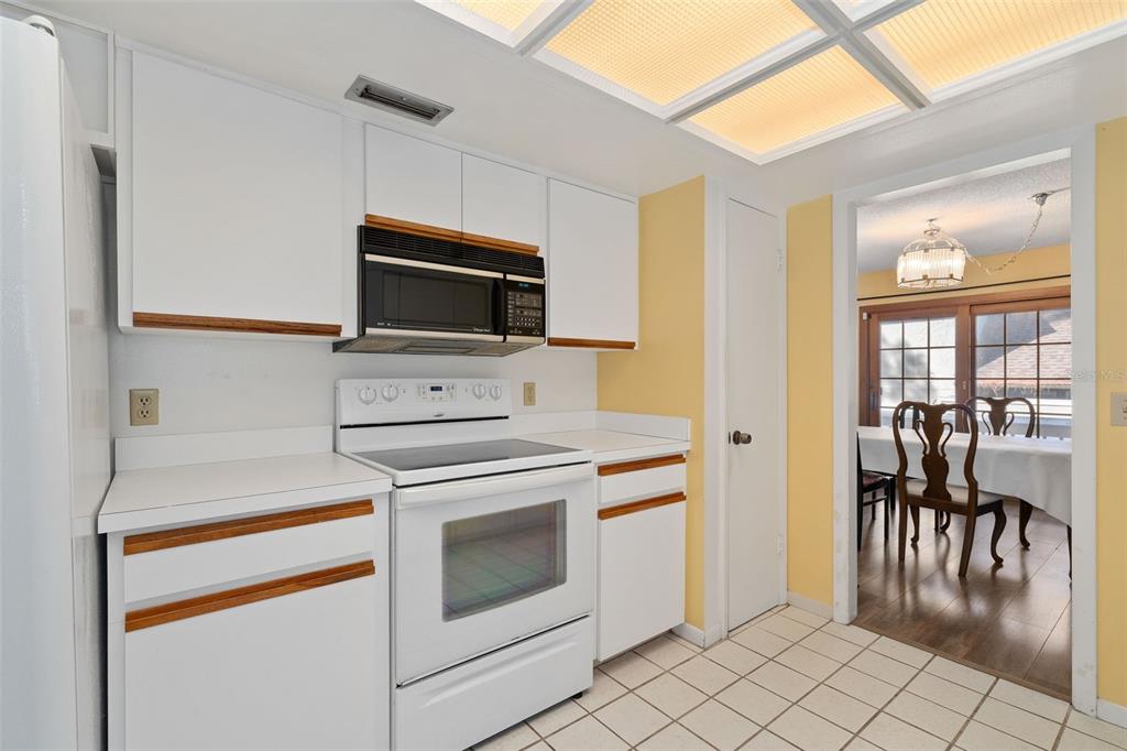 A kitchen with white cabinets, a white stove, and yellow walls leads to a dining area — 114 HIDDEN OAK DRIVE, LONGWOOD, FL