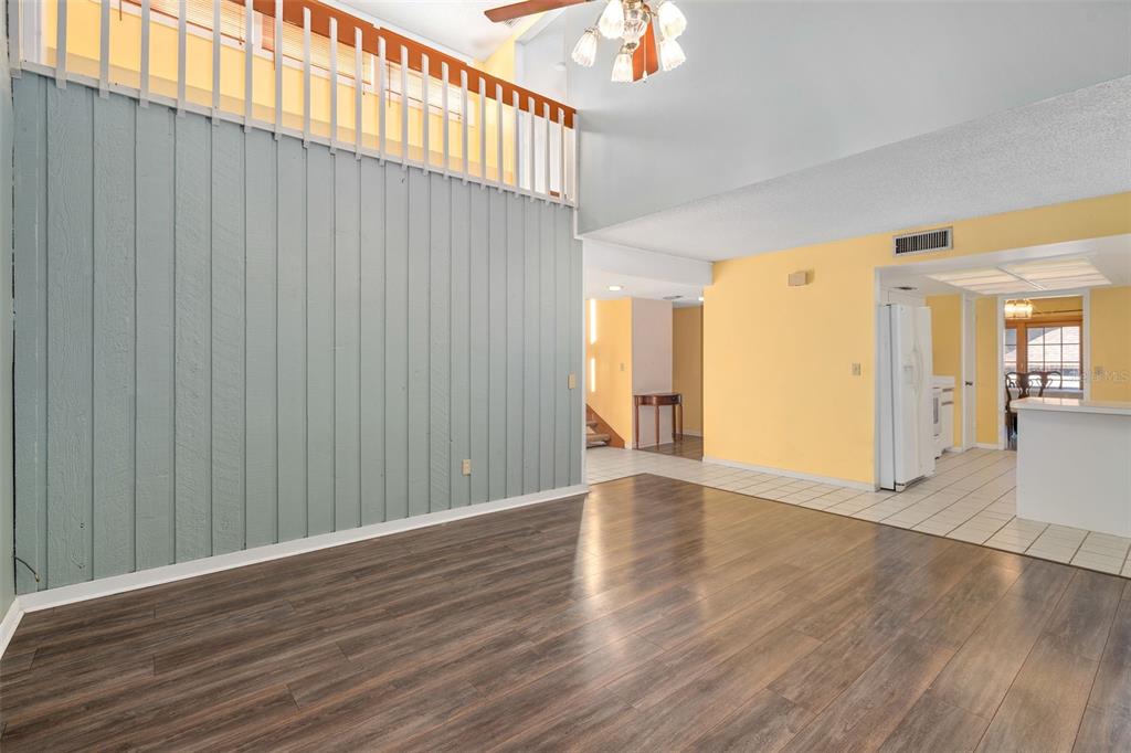 A living room with wood-look flooring, a light blue paneled wall, and a loft overlook — 114 HIDDEN OAK DRIVE, LONGWOOD, FL