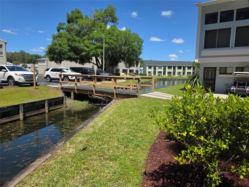 A wooden footbridge crosses a narrow canal between apartment buildings and a parking area — 1873 MAZO MANOR UNIT T9, LUTZ, FL