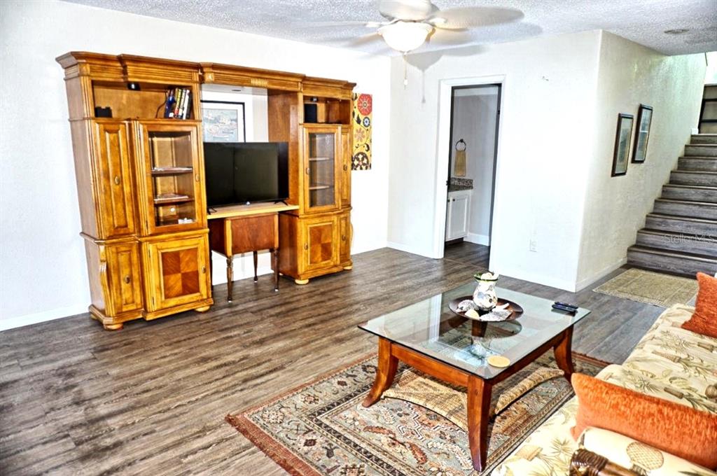 A living room features wood-look flooring, a large wooden entertainment center, and a staircase — 1873 MAZO MANOR UNIT T9, LUTZ, FL