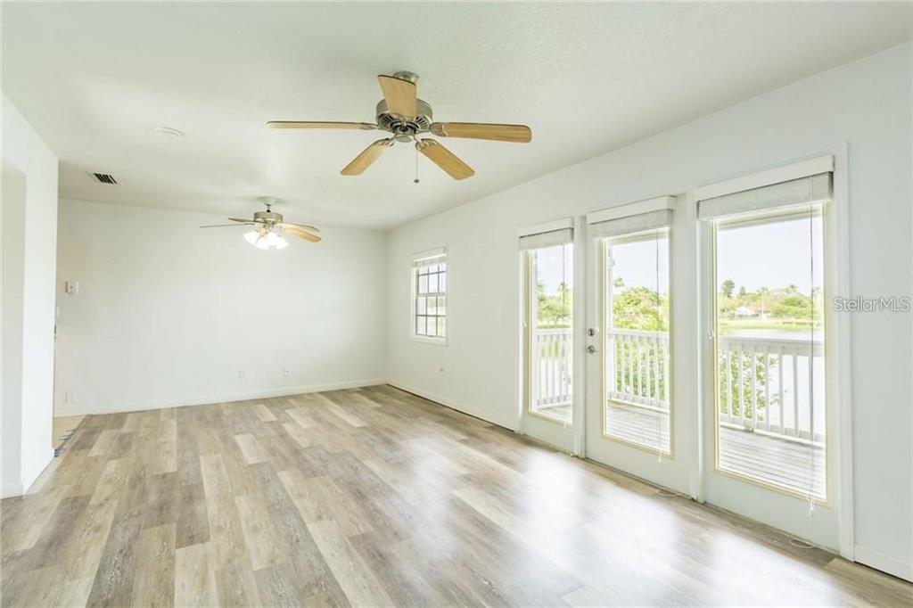 An empty room features light wood-look flooring, two ceiling fans, and glass doors to a deck — 4714 COBIA DRIVE SE UNIT D, ST PETERSBURG, FL