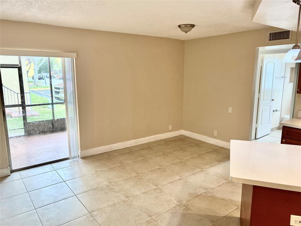 An empty dining area with beige tile floors, a sliding glass door, and a doorway — 4425 Treehouse Lane # A, Tamarac FL 33319, TAMARAC, FL