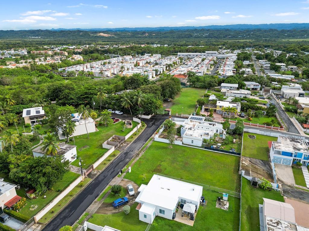 An aerial view shows a residential neighborhood with houses, green lawns, and a paved road — 690 LOS NABORIAS STREET, VEGA ALTA, PR