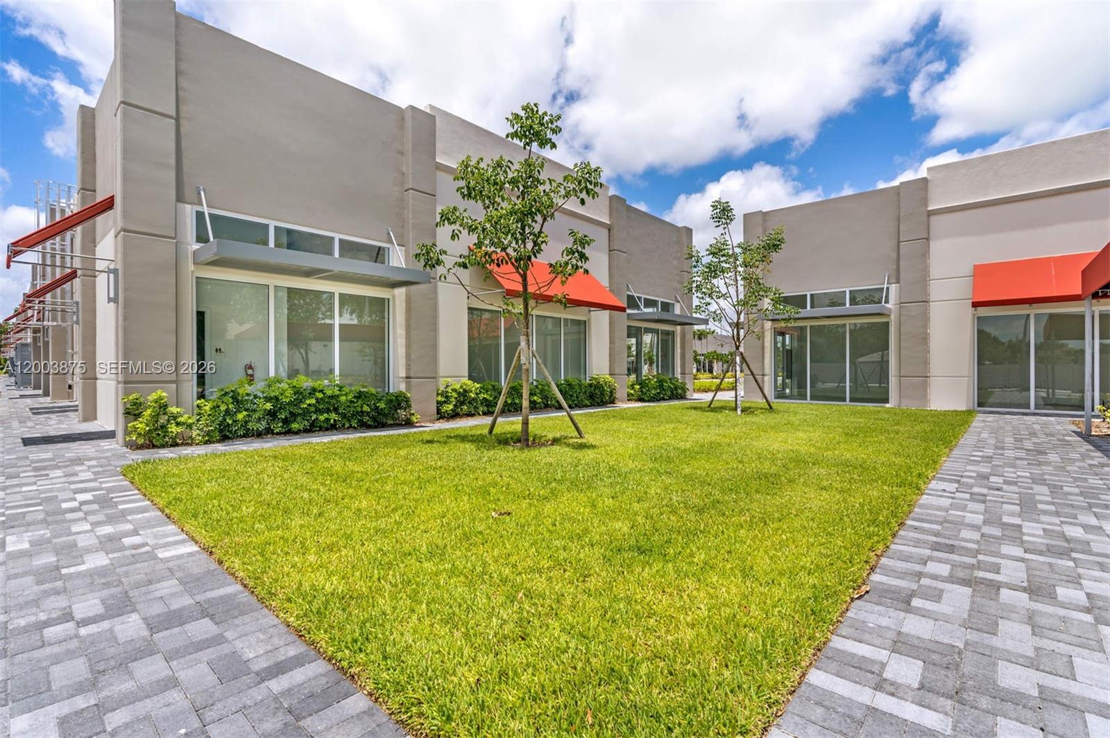 A grassy courtyard sits between modern commercial buildings with large windows and orange awnings — 9620 Stirling Rd # 101, Cooper City FL 33024, COOPER CITY, FL