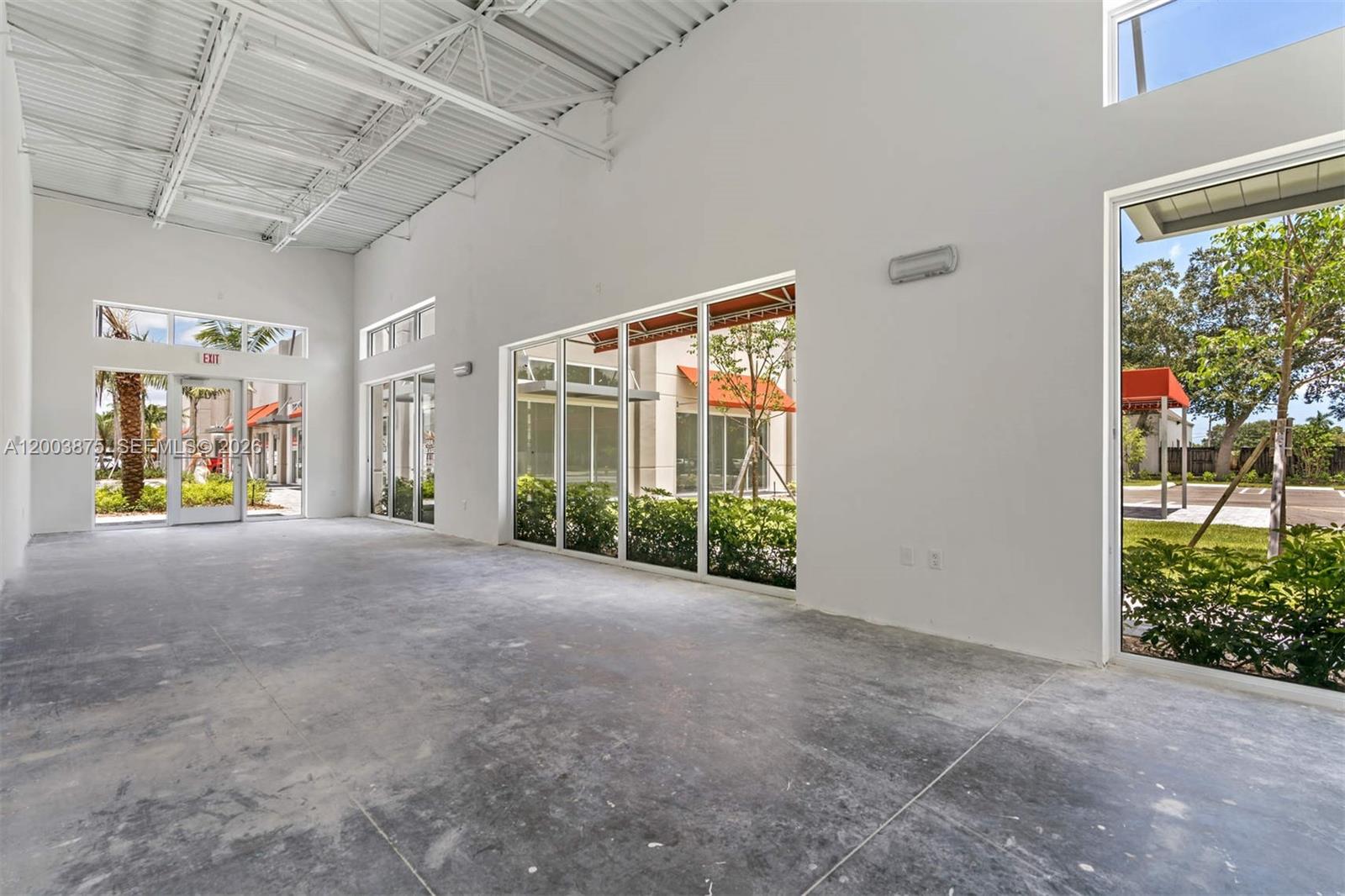 An empty commercial space features white walls, a high industrial ceiling, and large glass windows — 9620 Stirling Rd # 101, Cooper City FL 33024, COOPER CITY, FL