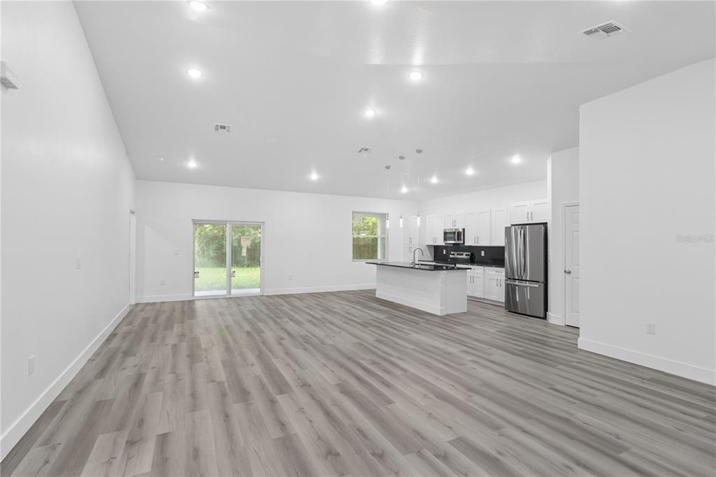 An open-concept living area features light wood-look flooring, white walls, and a modern kitchen — 1449 KATHLEEN ROAD, LAKELAND, FL