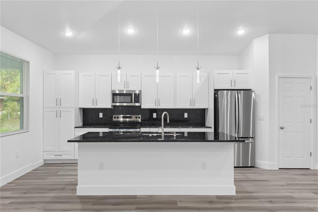 A modern kitchen features white cabinetry, black countertops, stainless steel appliances, and a central island — 1449 KATHLEEN ROAD, LAKELAND, FL
