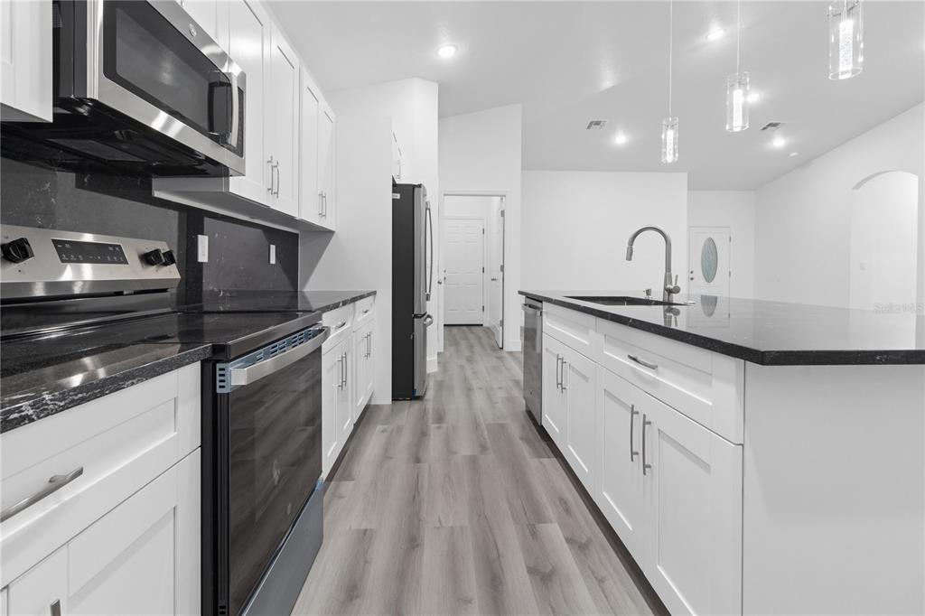 A modern kitchen features white cabinets, black countertops, stainless steel appliances, and light wood flooring — 1449 KATHLEEN ROAD, LAKELAND, FL