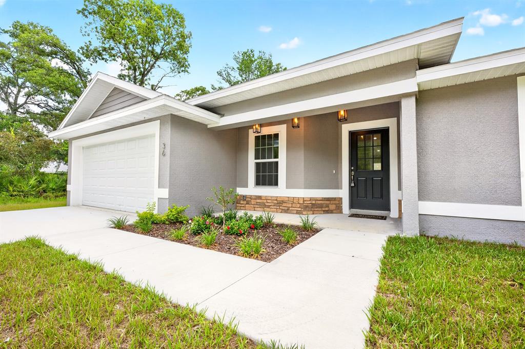 A gray single-story house features a white garage door, a front porch, and stone accents — 36 FISHER LANE COURSE, OCKLAWAHA, FL