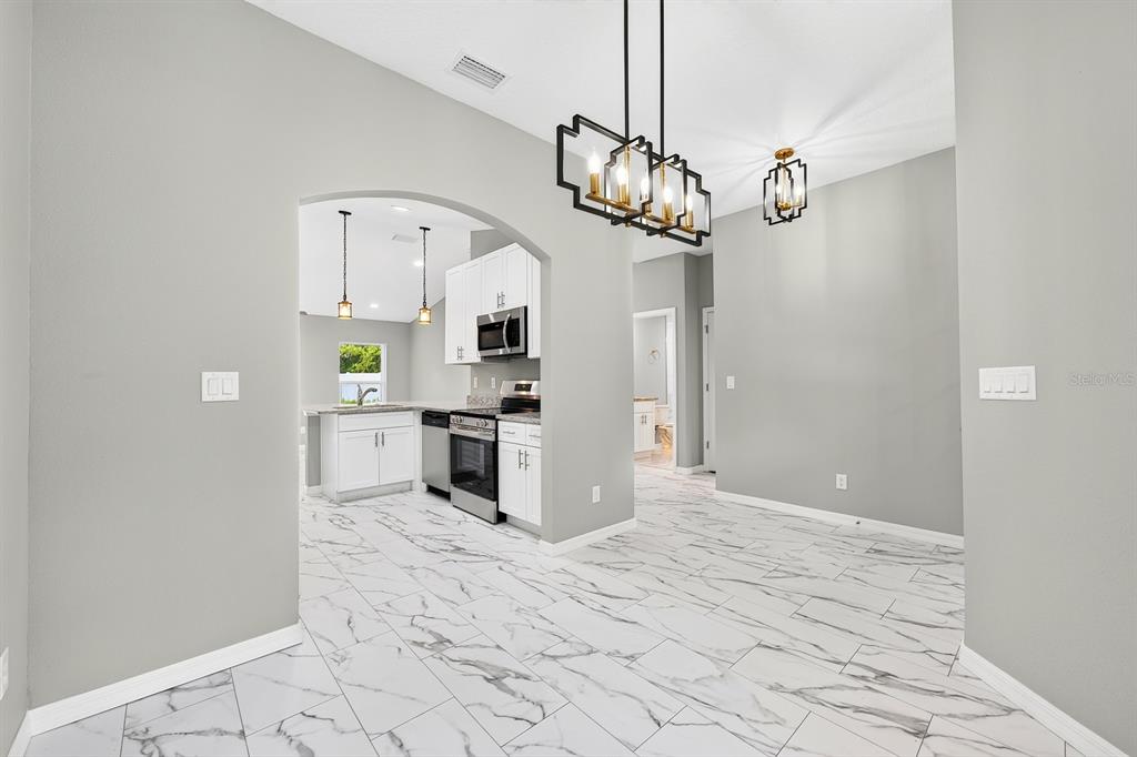 A dining area with marble-look tile flooring leads through an arched opening into a kitchen — 36 FISHER LANE COURSE, OCKLAWAHA, FL