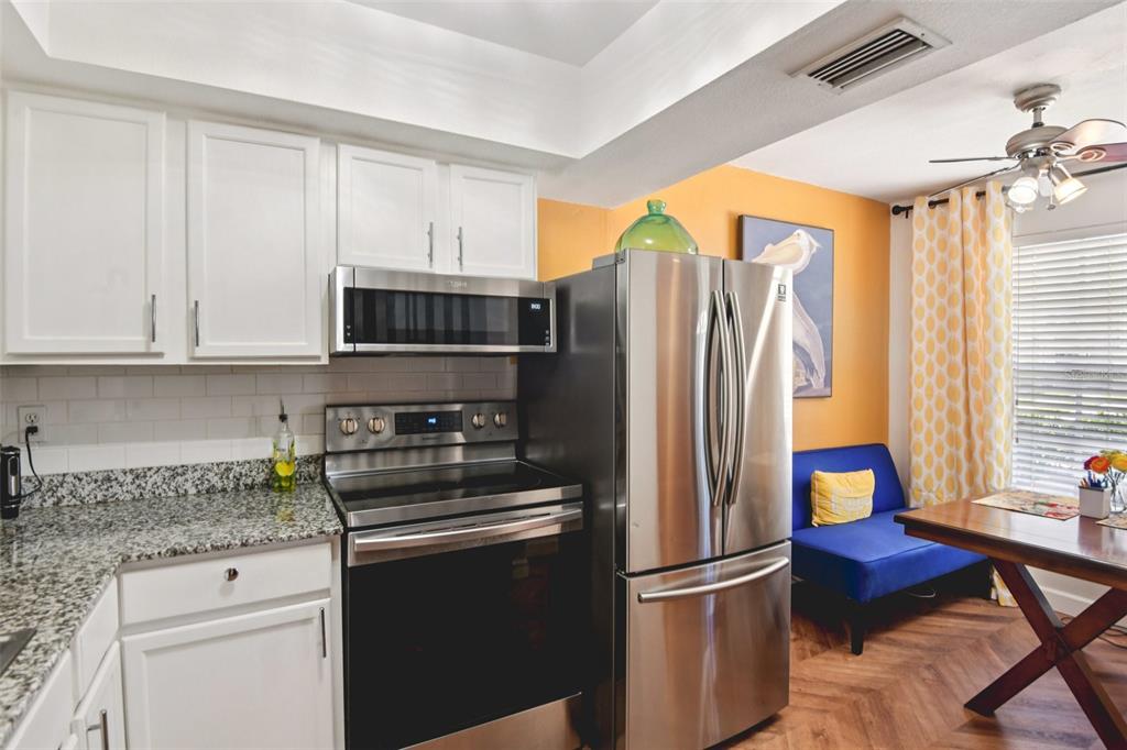 A kitchen with white cabinets, stainless steel appliances, granite countertops, and an adjacent dining area — 14019 NOTREVILLE WAY, TAMPA, FL