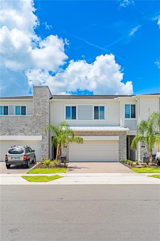 A two-story townhouse with a stone facade, a two-car garage, and a palm tree — 294 BOGEY DRIVE, DAVENPORT, FL