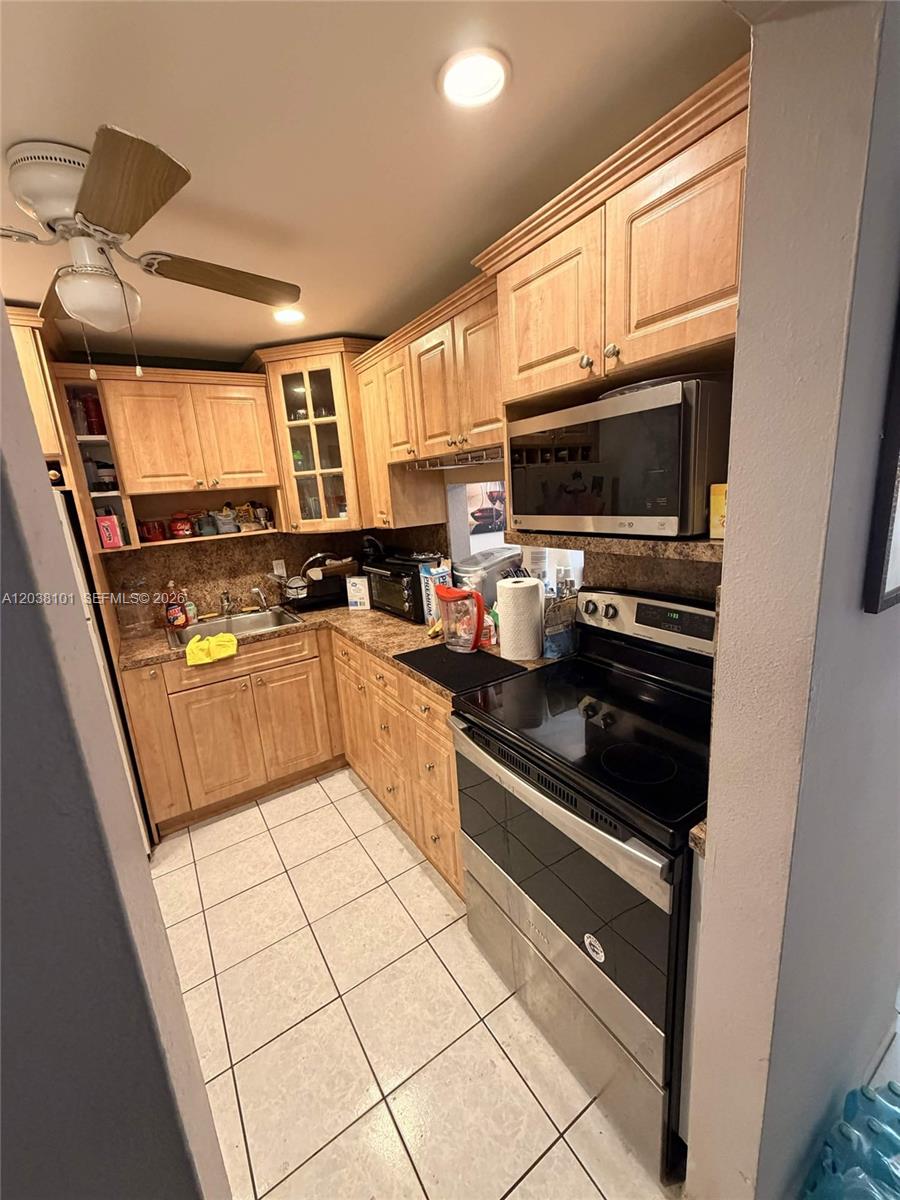 A kitchen features light wood cabinets, a black stove, a microwave, and tiled flooring — 9974 SW 88th St # 1011, Miami FL 33176, MIAMI, FL