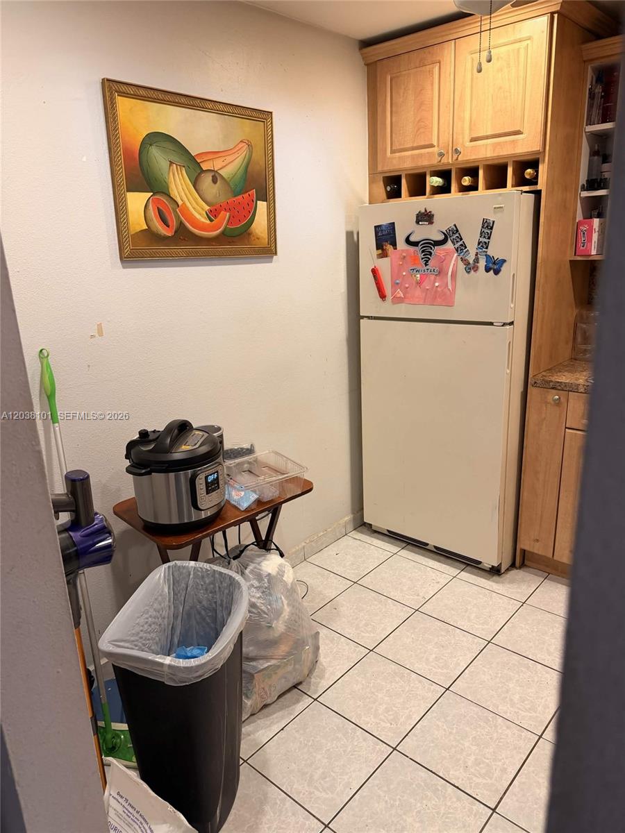 A kitchen area features a white refrigerator, wooden cabinets, a small table, and tiled floors — 9974 SW 88th St # 1011, Miami FL 33176, MIAMI, FL