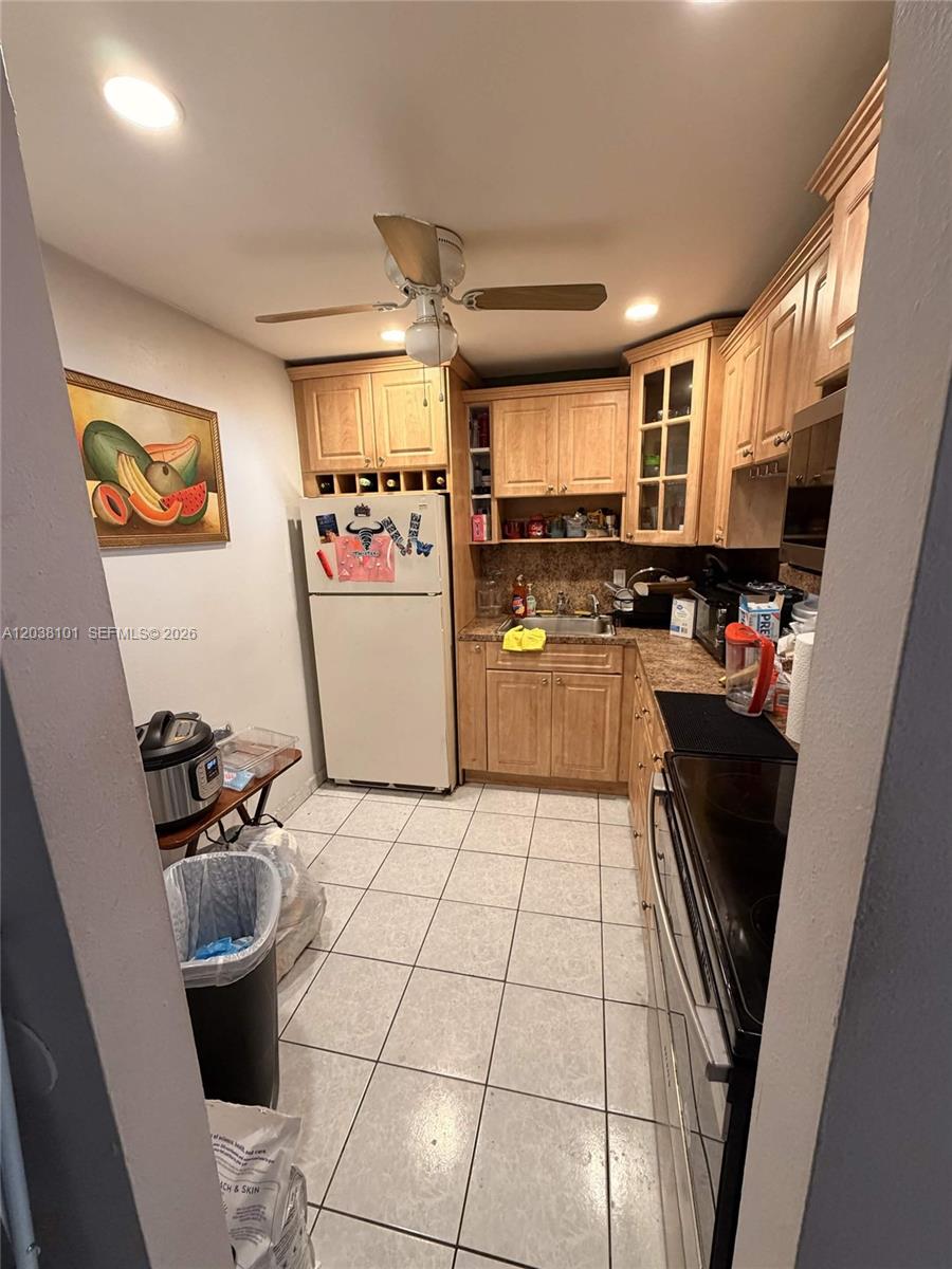 A galley-style kitchen features light wood cabinets, white tile flooring, and a white refrigerator — 9974 SW 88th St # 1011, Miami FL 33176, MIAMI, FL