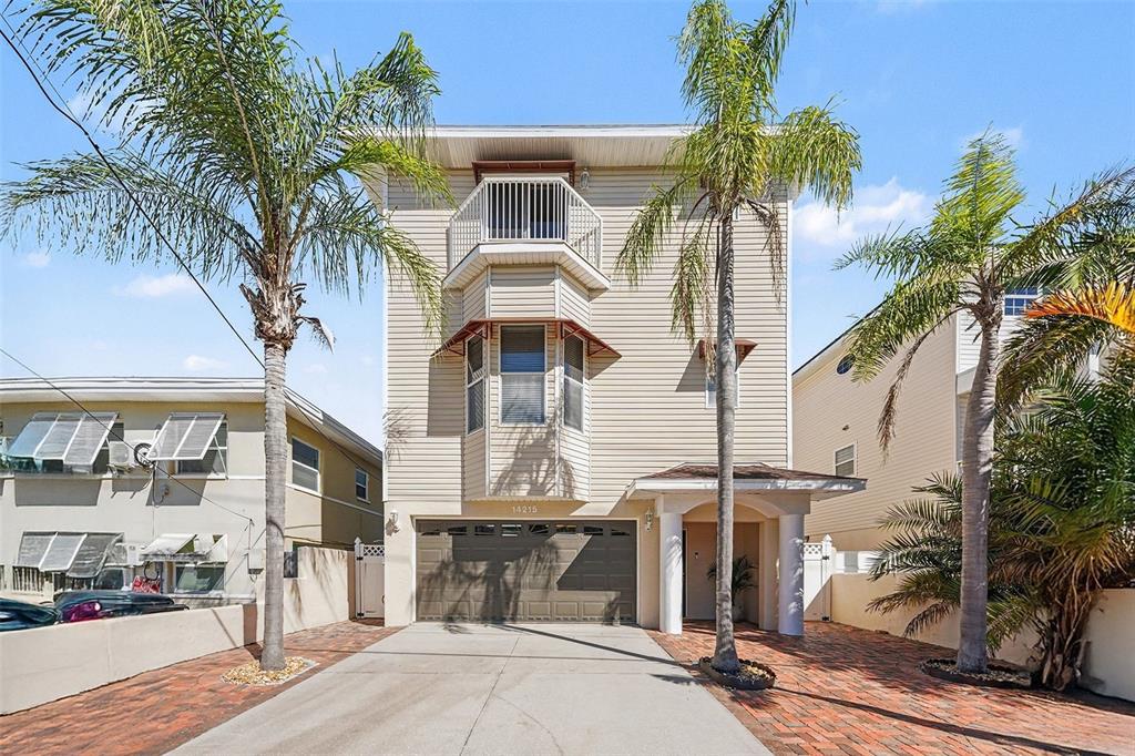 A three-story beige house with a garage and two palm trees in the front yard — 14215 N BAYSHORE DRIVE, MADEIRA BEACH, FL