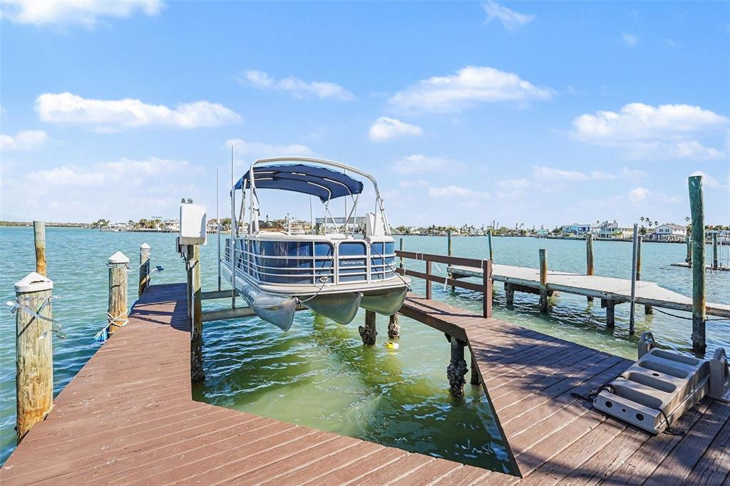 A pontoon boat sits on a mechanical lift attached to a wooden dock — 14215 N BAYSHORE DRIVE, MADEIRA BEACH, FL