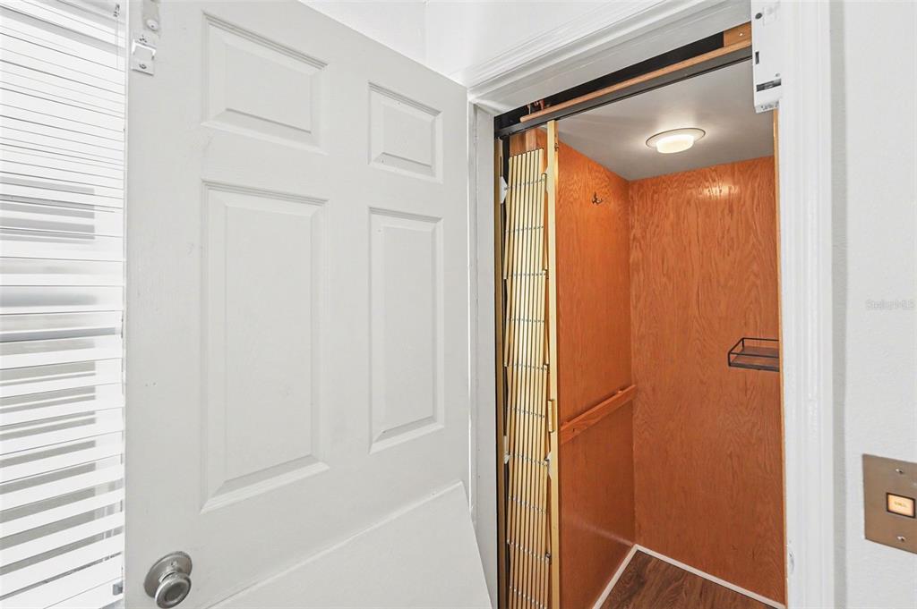 An open white door reveals a small residential elevator with wood-paneled walls and a folding gate — 14215 N BAYSHORE DRIVE, MADEIRA BEACH, FL