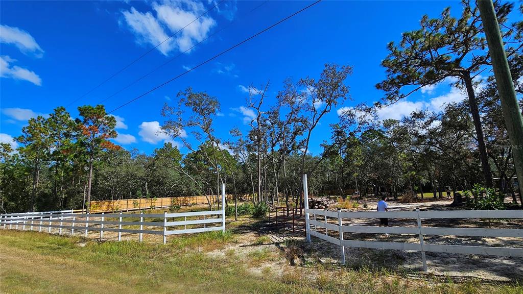 A white split-rail fence encloses a sandy, partially wooded lot under a bright blue sky — 16266 NIGHT HERON ROAD, WEEKI WACHEE, FL