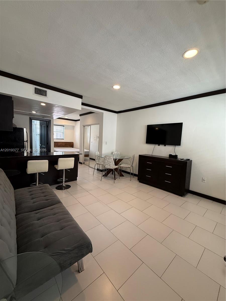 This open-concept living area features white tile floors, a kitchen breakfast bar, and a television — 1545 Drexel Ave # 422, Miami Beach FL 33139, MIAMI BEACH, FL