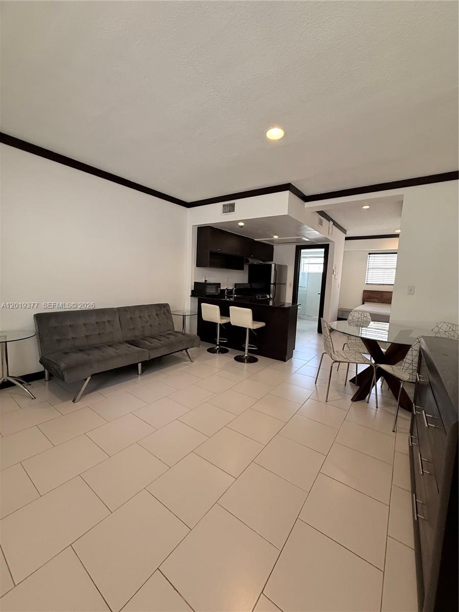 A living area with a grey sofa, kitchen island, and dining table on tiled floors — 1545 Drexel Ave # 422, Miami Beach FL 33139, MIAMI BEACH, FL