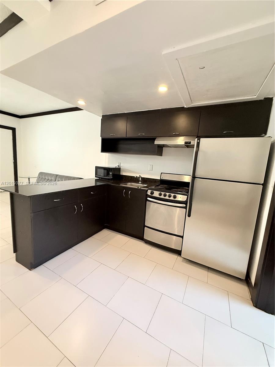 A kitchen features dark cabinets, stainless steel appliances, and white tile flooring — 1545 Drexel Ave # 422, Miami Beach FL 33139, MIAMI BEACH, FL
