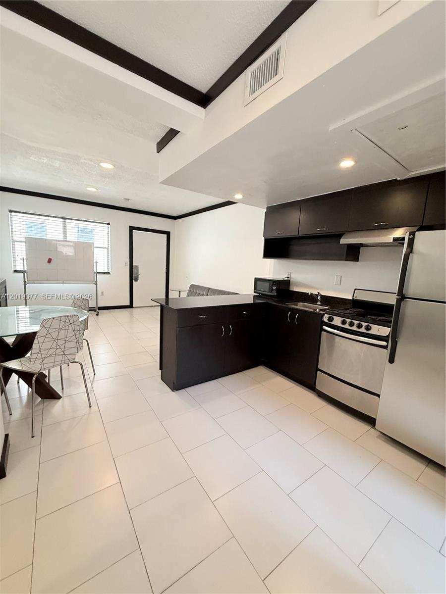 A kitchen with dark cabinets and stainless steel appliances opens into a tiled living area — 1545 Drexel Ave # 422, Miami Beach FL 33139, MIAMI BEACH, FL