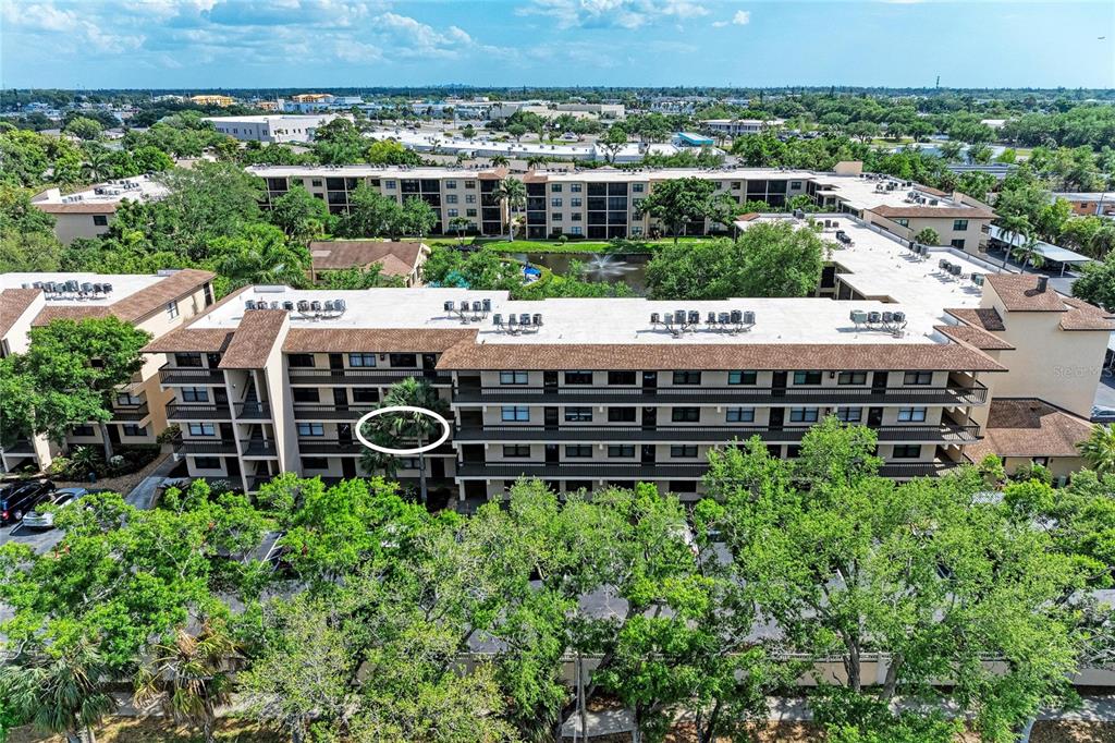 An aerial view shows a multi-story apartment building with a circled balcony and surrounding trees — 625 30TH AVENUE W UNIT G203, BRADENTON, FL