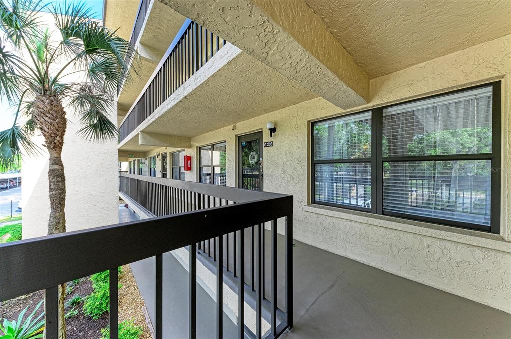 An exterior view of an apartment building walkway featuring a palm tree and unit G203 — 625 30TH AVENUE W UNIT G203, BRADENTON, FL
