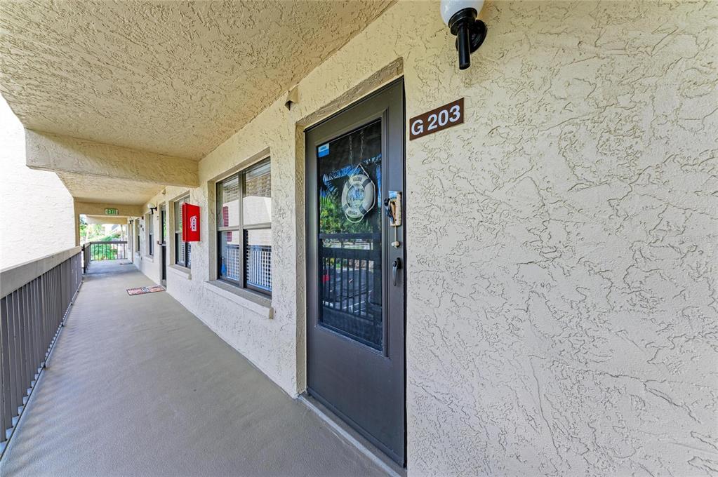An exterior view of a second-floor apartment walkway featuring a door labeled G 203 — 625 30TH AVENUE W UNIT G203, BRADENTON, FL