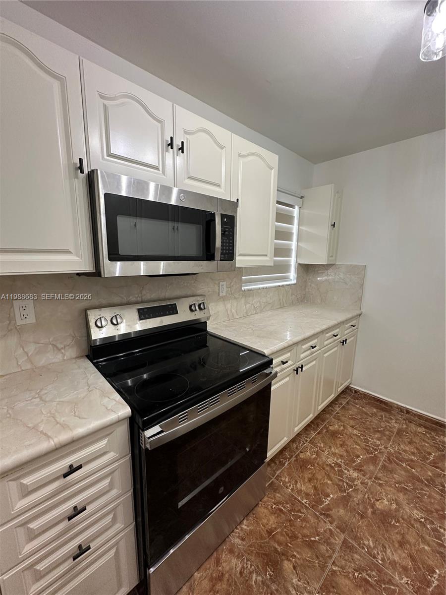 A kitchen features white cabinets, stainless steel appliances, marble-patterned countertops, and brown tiled flooring — 6091 W 22nd Ct # 408, Hialeah FL 33016, HIALEAH, FL